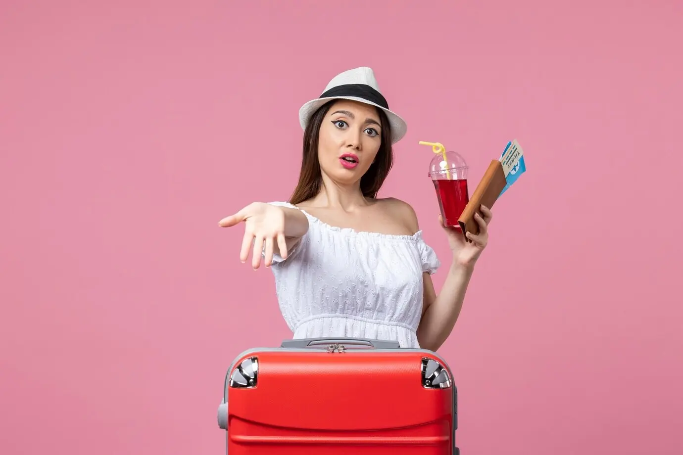 Вид спереди: молодая женщина на фоне розовой стены, в отпуске, держит билеты и сок; лето, поездка, отдых, путешествие.