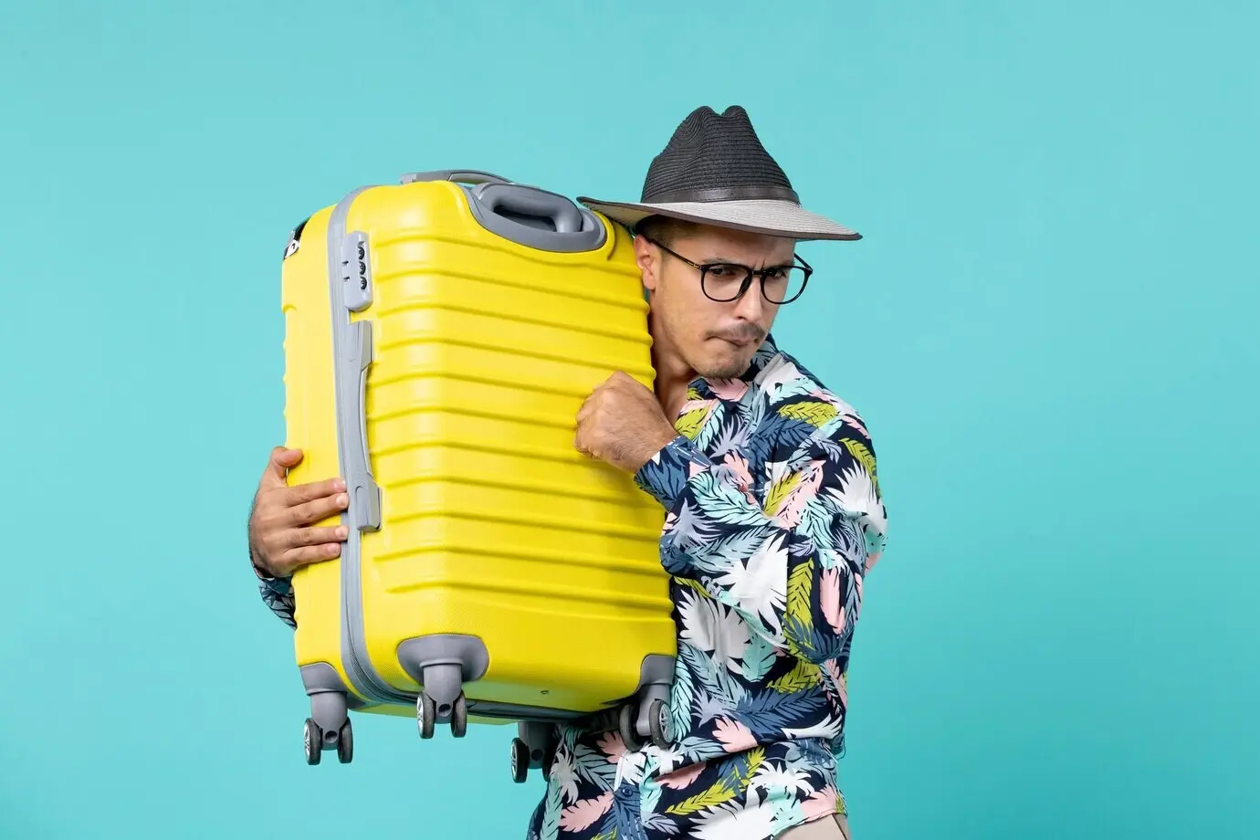 Молодой мужчина, вид спереди, отправляющийся в отпуск и держащий свою жёлтую сумку на светло-голубом фоне.